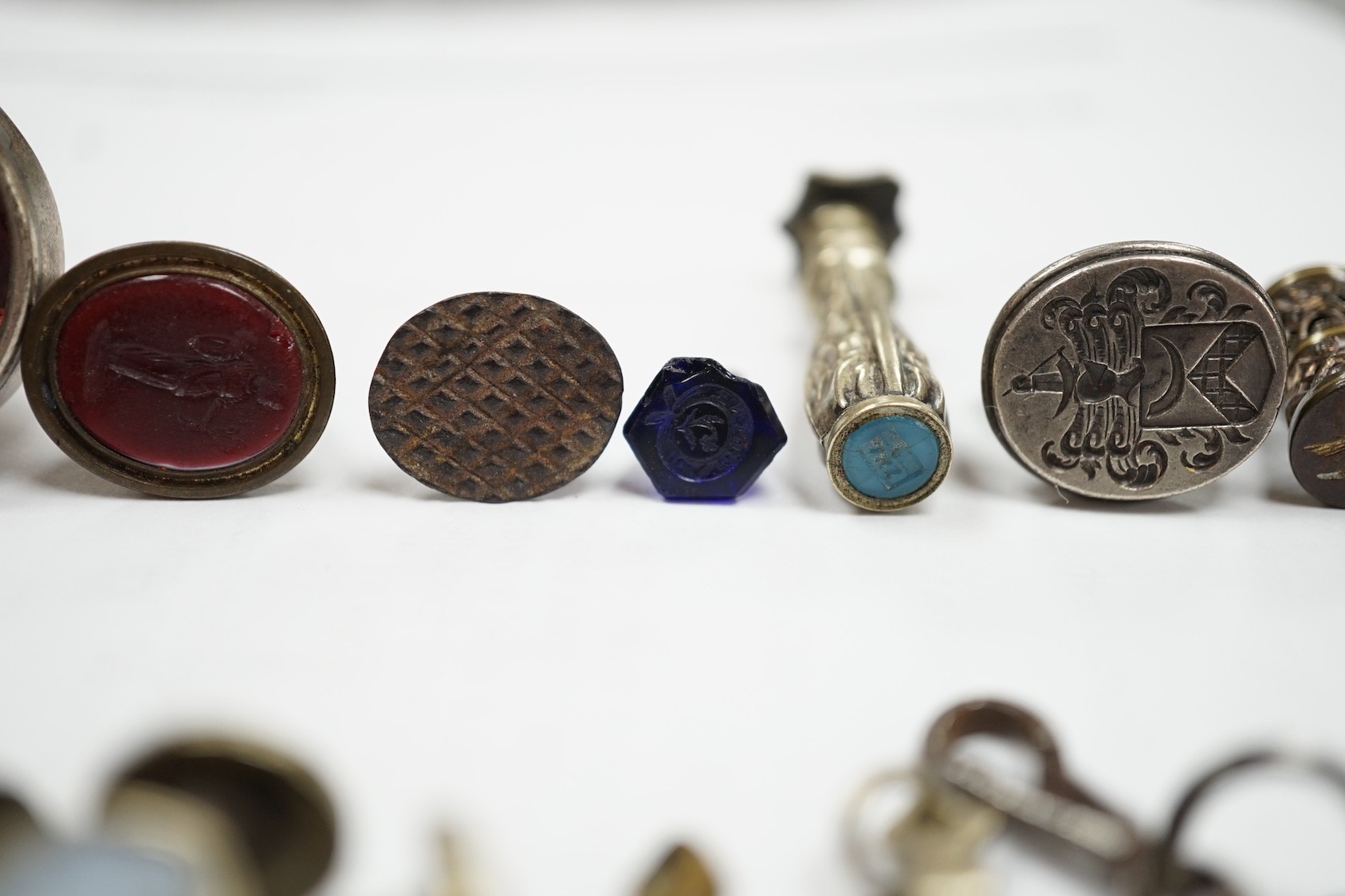 A group of twenty-five steel, gilt metal or nickel fob or desk seals, mostly 19th-century, including a steel swivel seal, a seal with boxwood finial modelled as a hand holding a ball and a nickel multi seal